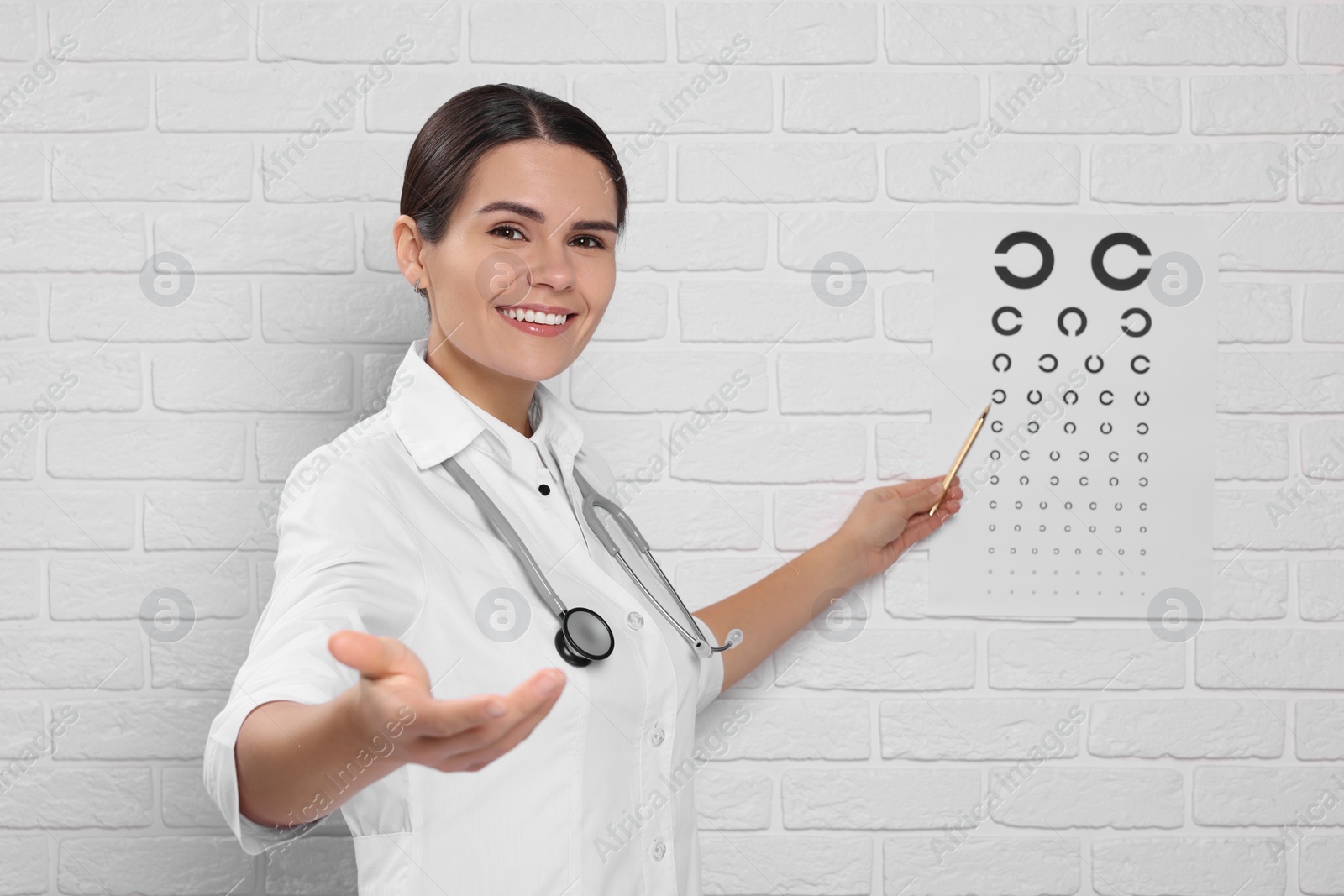 Photo of Ophthalmologist pointing at vision test chart on white brick wall