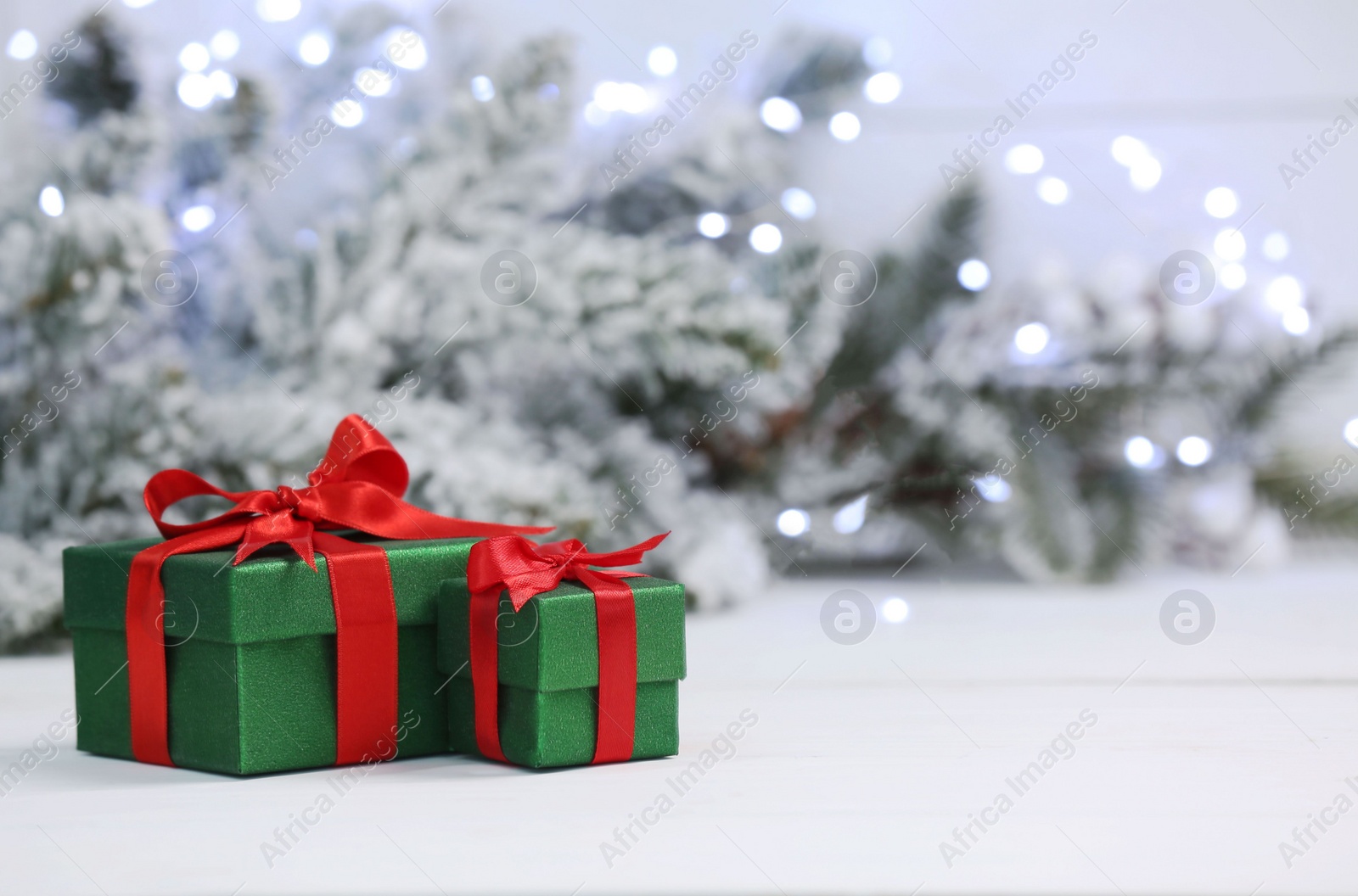 Photo of Beautiful gift boxes on white table against blurred festive lights, space for text. Christmas present