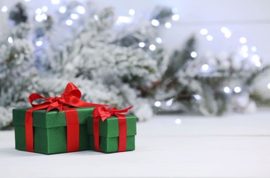 Photo of Beautiful gift boxes on white table against blurred festive lights, space for text. Christmas present