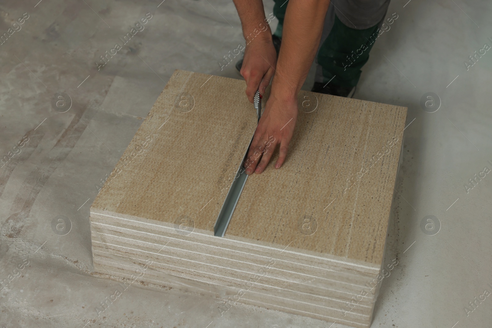 Photo of Worker cutting PVC ceiling tile on floor, closeup