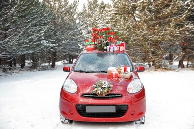 Car with Christmas tree, wreath and gifts in snowy forest on winter day