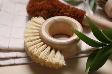 Photo of Cleaning brushes, towel and green leaves on beige background, closeup