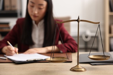 Notary signing document at wooden table in office, focus on scales