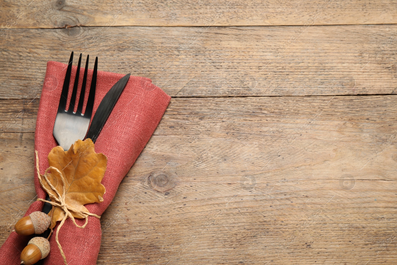 Photo of Top view of cutlery with acorns, autumn leaf and napkin on wooden table, space for text. Thanksgiving Day