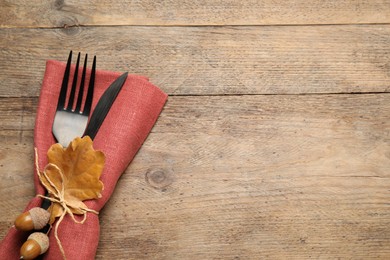 Photo of Top view of cutlery with acorns, autumn leaf and napkin on wooden table, space for text. Thanksgiving Day