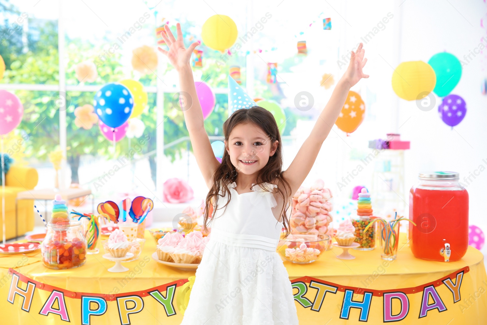 Photo of Cute little girl near table with treats at birthday party indoors
