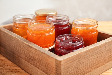 Photo of Jars with different sweet jam in wooden crate, closeup