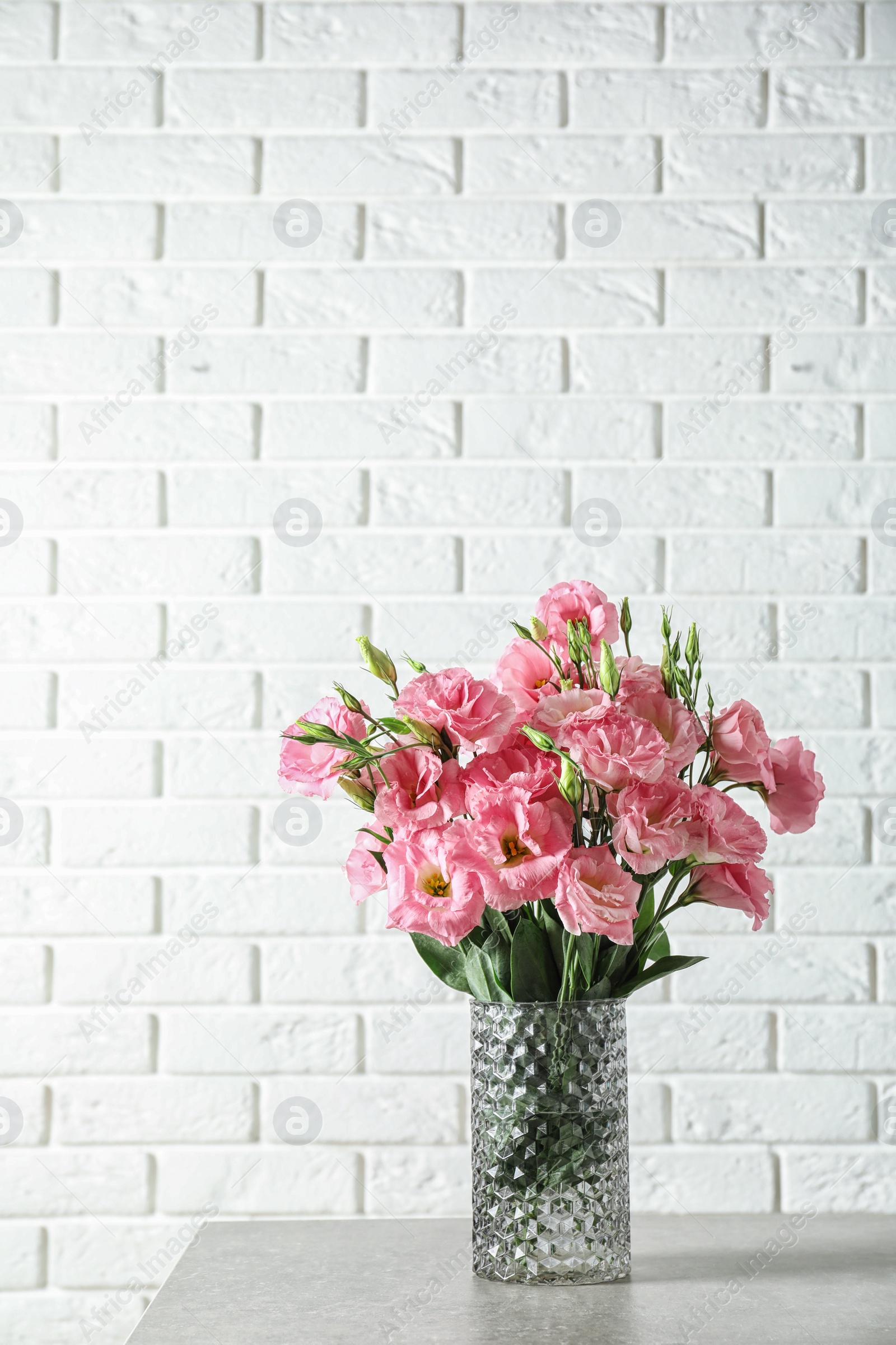 Photo of Vase with beautiful Eustoma flowers on table against brick wall