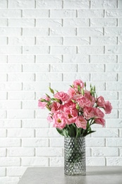 Photo of Vase with beautiful Eustoma flowers on table against brick wall