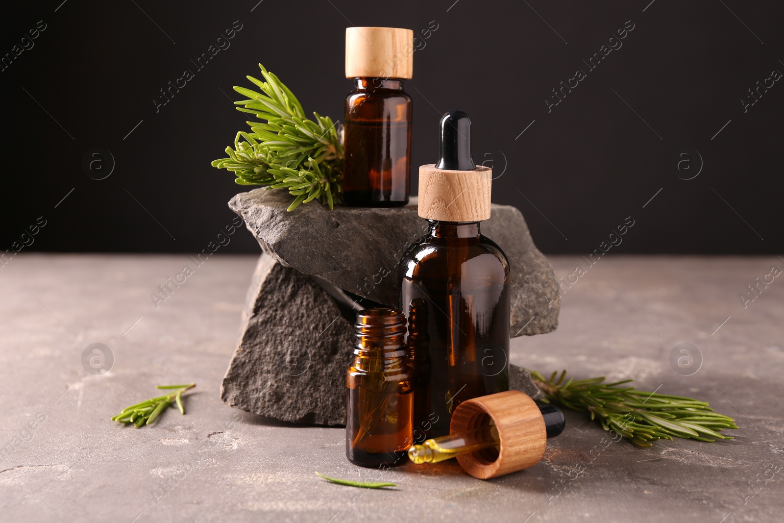 Photo of Essential oil in bottles, dropper and rosemary on grey table