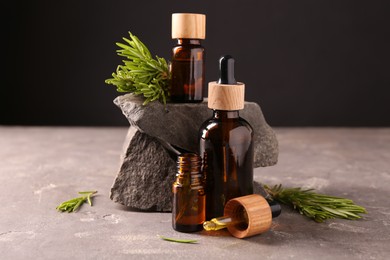 Photo of Essential oil in bottles, dropper and rosemary on grey table