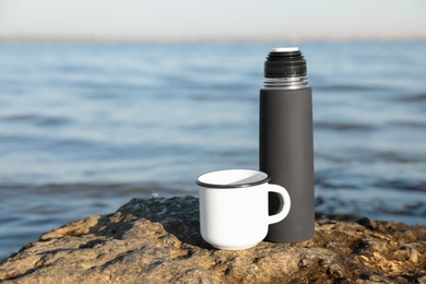 Photo of Modern black thermos and cup on beach. Space for text
