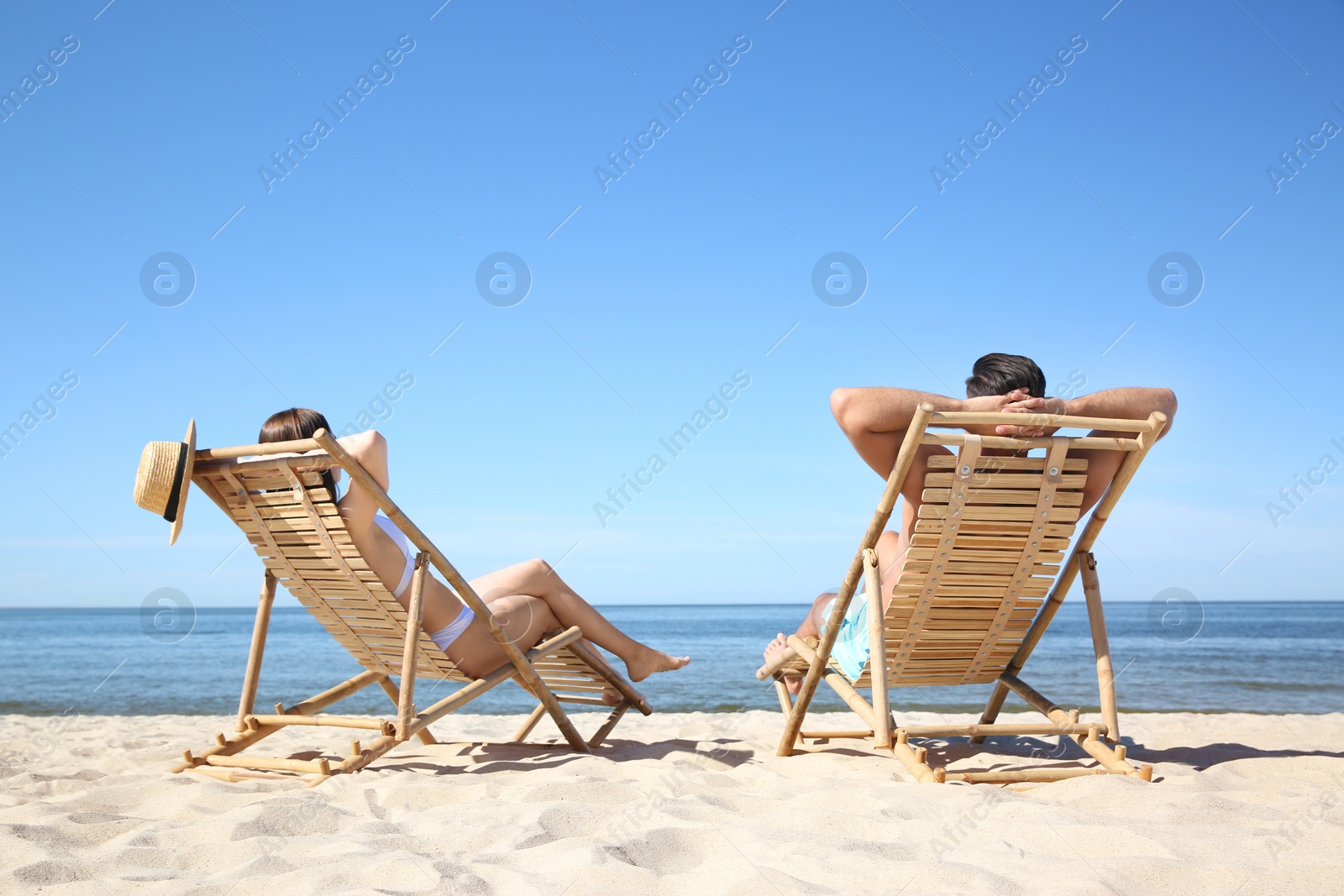 Photo of Woman in bikini and her boyfriend on deck chairs at beach. Lovely couple