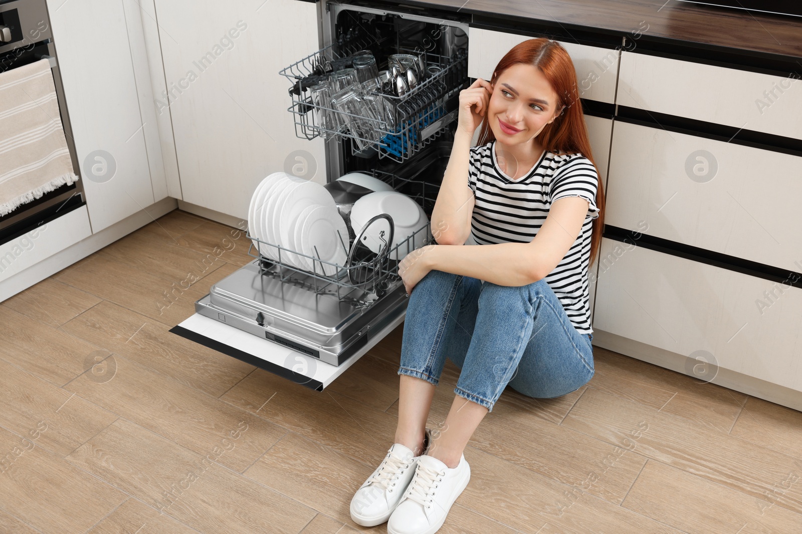 Photo of Beautiful woman sitting near open dishwasher in kitchen