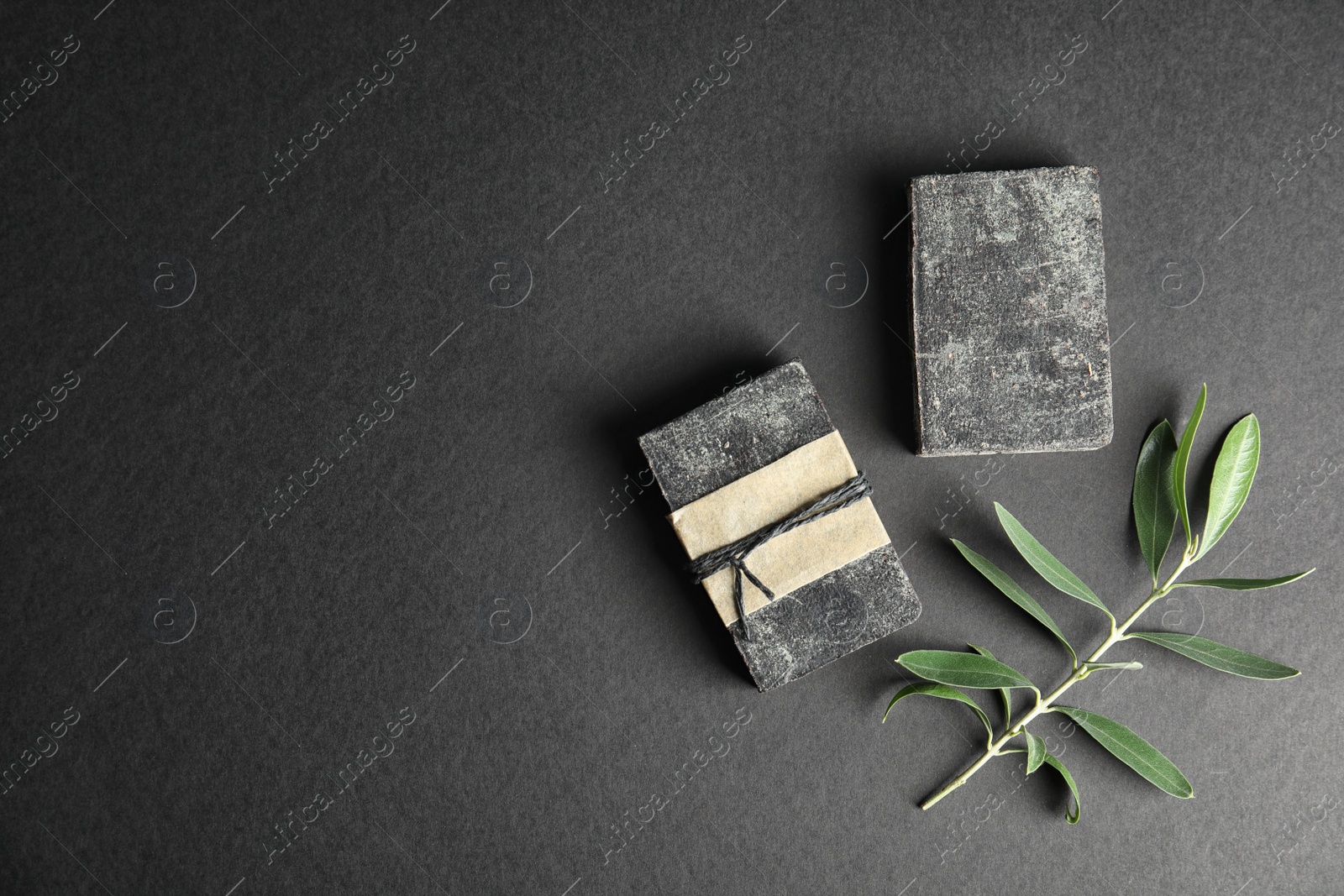 Photo of Handmade soap bars with olive twig and space for text on black background, top view