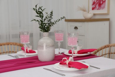 Photo of Table setting. Glasses of tasty beverage, plates, pink napkins and vase with green branches in dining room