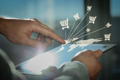 Image of Man using tablet for online purchases on blurred background, closeup. Illustration of world map and shopping cart icons above device screen