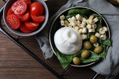 Delicious burrata cheese served with olives, croutons, basil and tomatoes on wooden table, top view