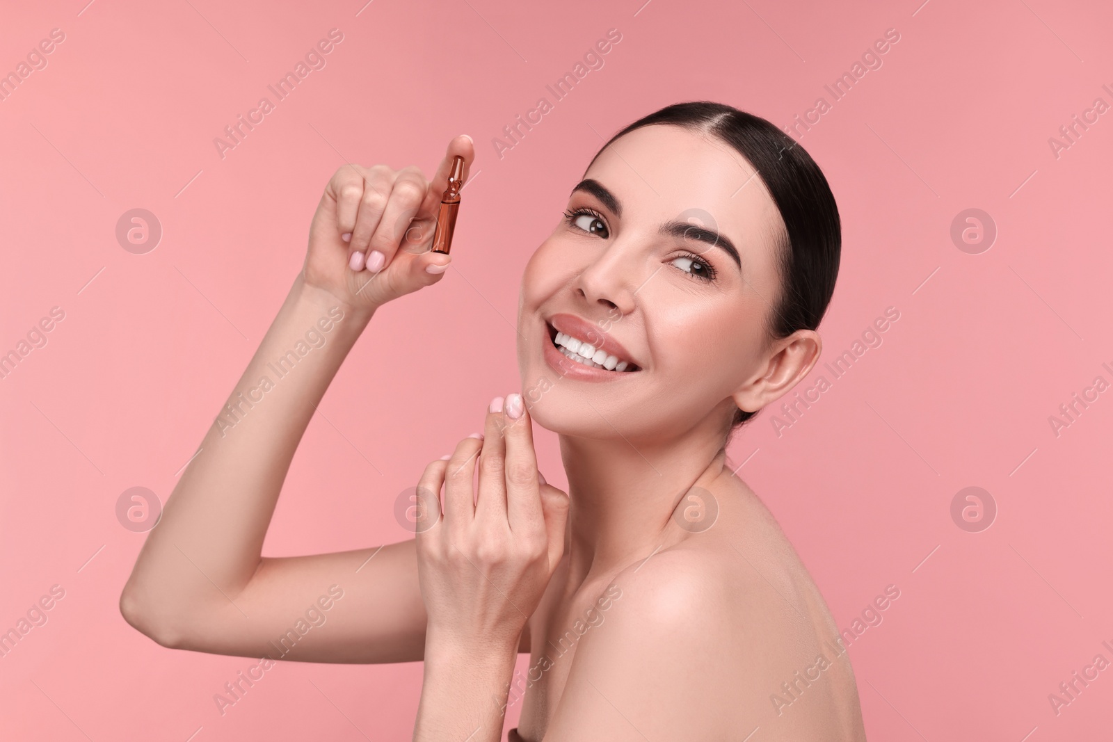 Photo of Beautiful young woman holding skincare ampoule on pink background