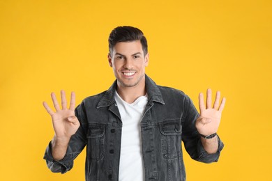 Photo of Man showing number eight with his hands on yellow background