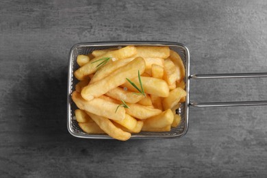 Photo of Metal basket with tasty French fries and rosemary on grey table, top view