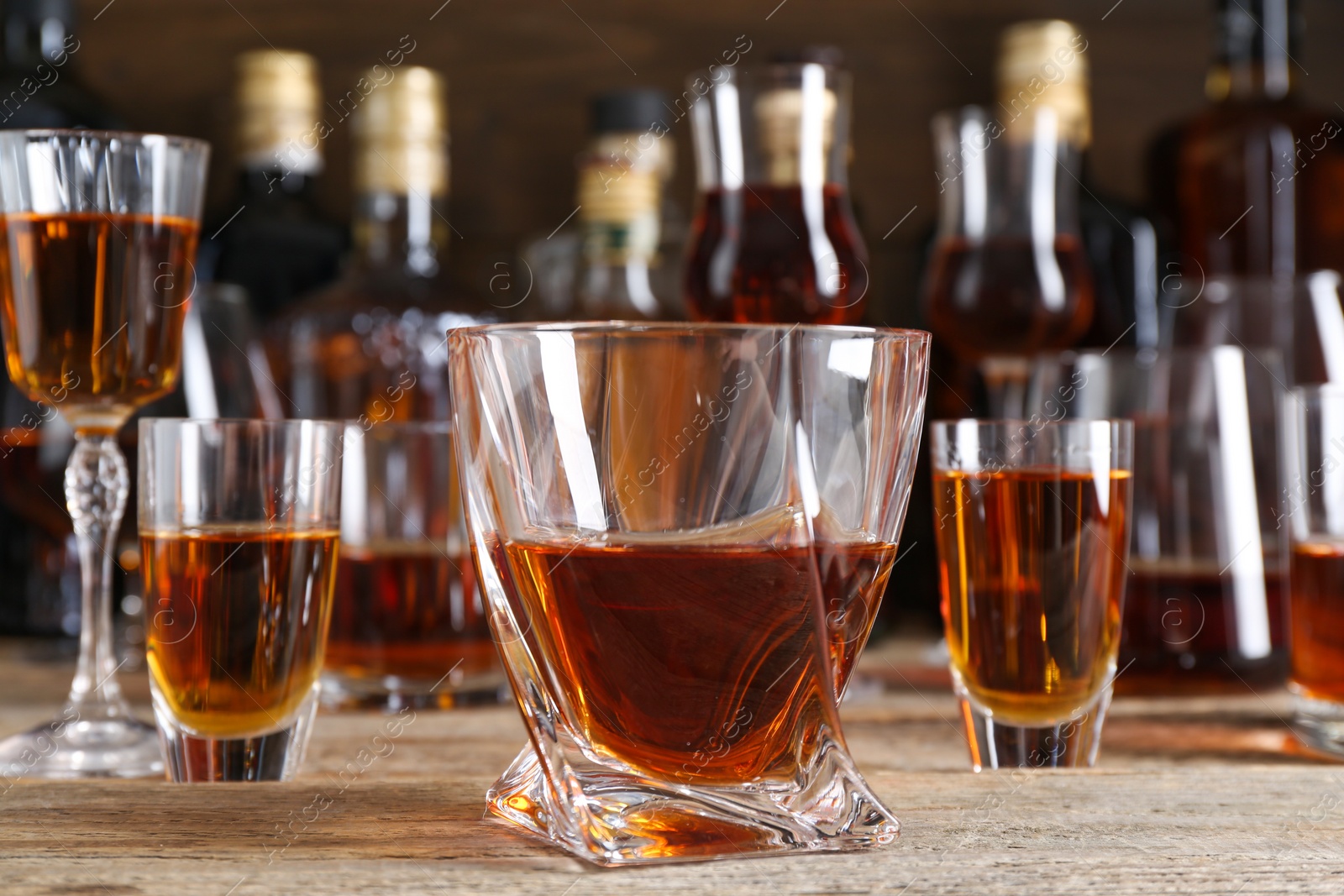 Photo of Different delicious liqueurs in glasses and bottles on wooden table