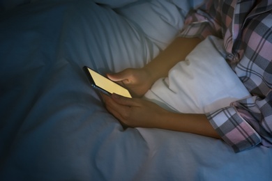 Photo of Woman using smartphone in bed at night, closeup. Nomophobia and sleeping disorder problem