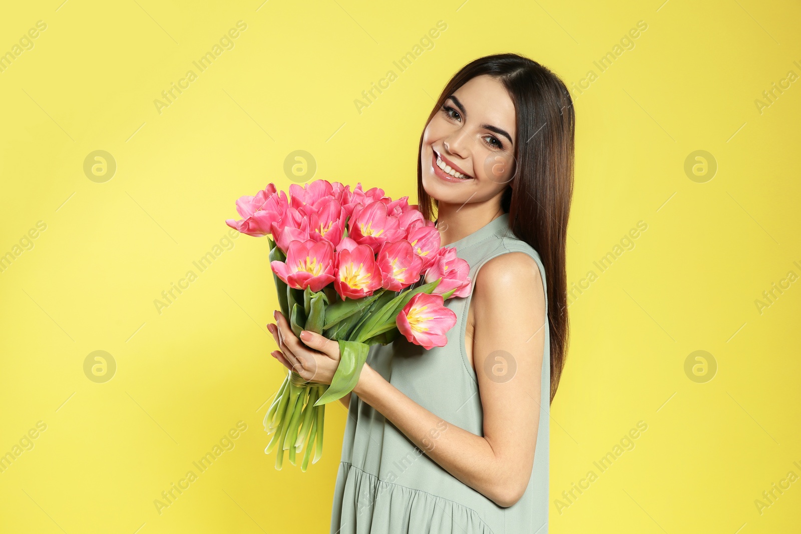 Photo of Portrait of beautiful smiling girl with spring tulips on yellow background. International Women's Day