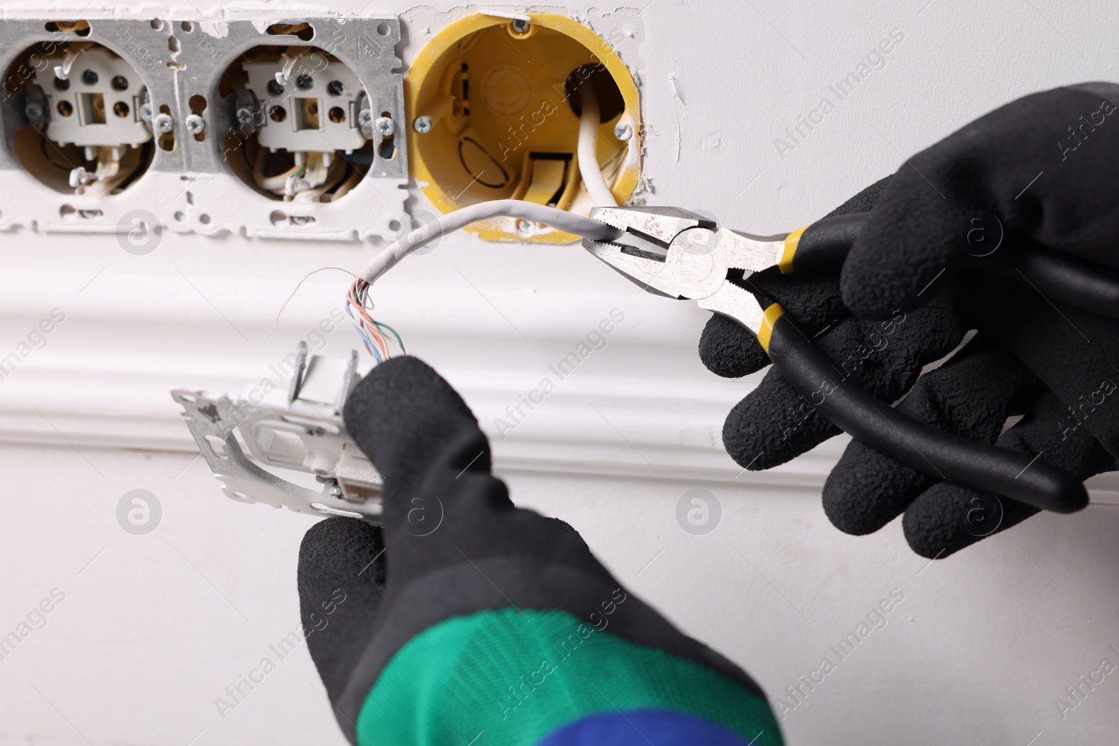 Photo of Professional repairman fixing power sockets with pliers indoors, closeup