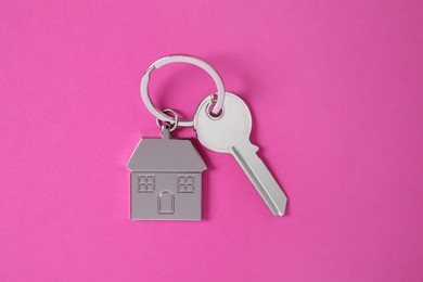 Photo of Key with keychain in shape of house on pink background, top view
