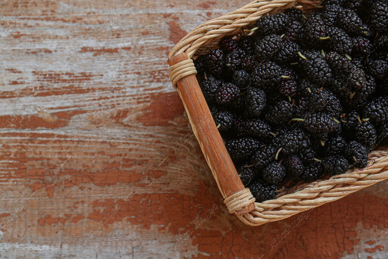 Photo of Wicker basket with delicious ripe black mulberries on wooden table, top view. Space for text