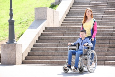 Photo of Preteen boy in wheelchair with his mother outdoors