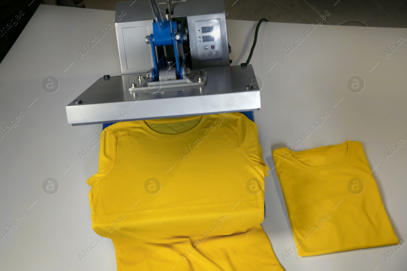 Photo of Printing logo. Heat press with yellow t-shirts on white table