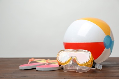 Photo of Inflatable ball, flip flops and mask on table against light background. Beach objects