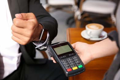 Photo of Man making payment with smart watch in cafe, closeup