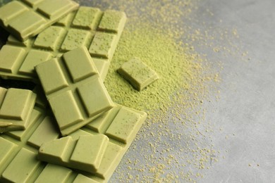 Pieces of tasty matcha chocolate bars and powder on grey table, closeup. Space for text