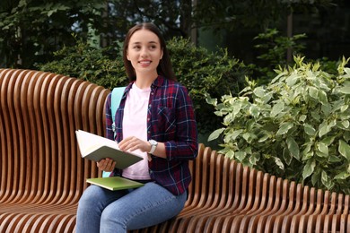 Photo of Happy young student studying with notebooks on bench outdoors, space for text