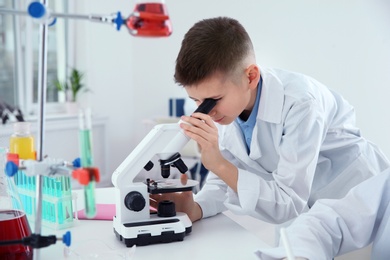 Photo of Schoolboy looking through microscope at table in chemistry class