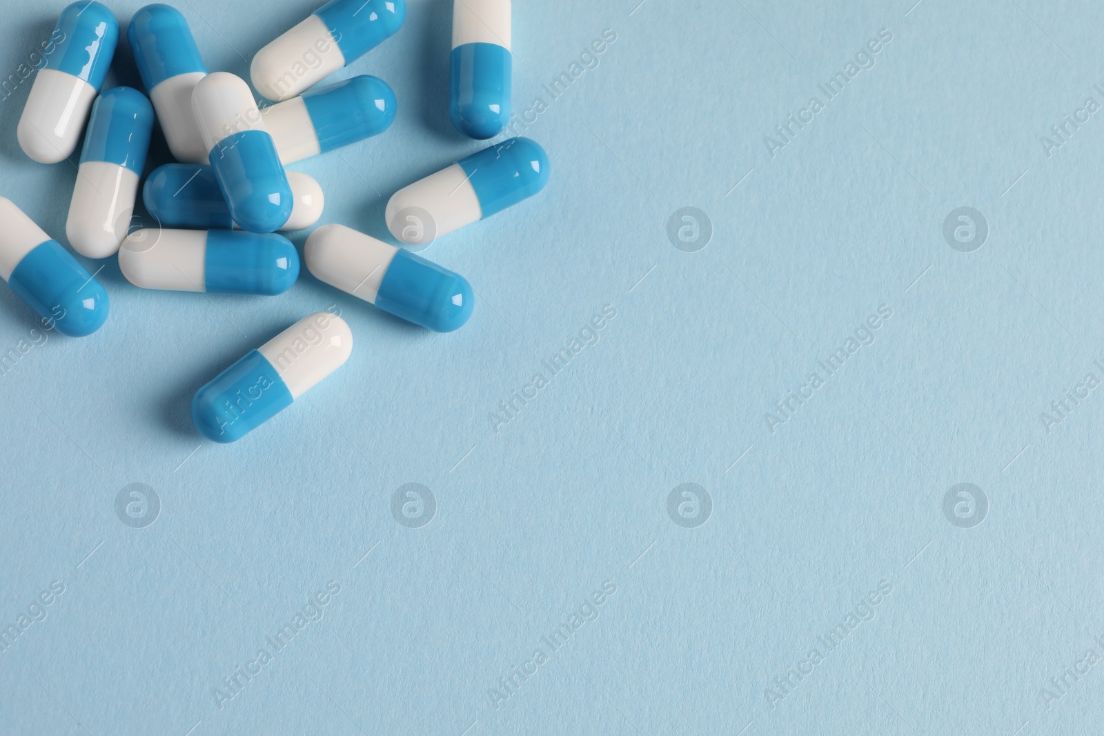 Photo of Pile of pills on light blue background, flat lay. Space for text