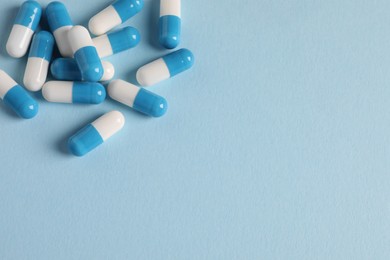 Pile of pills on light blue background, flat lay. Space for text