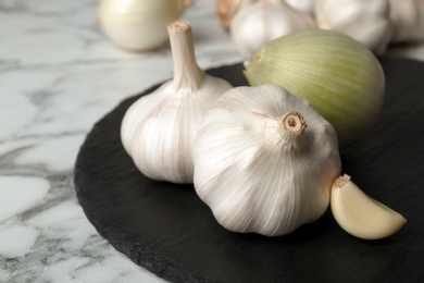 Photo of Slate plate with garlic and onion on marble table, closeup