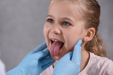Photo of Doctor in medical gloves examining girl`s oral cavity on grey background, closeup