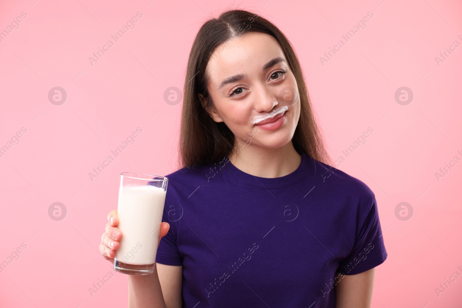 Photo of Cute woman with milk mustache holding glass of tasty dairy drink on pink background