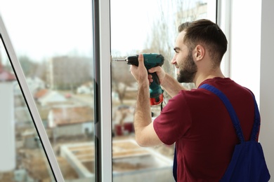 Construction worker using drill while installing window indoors