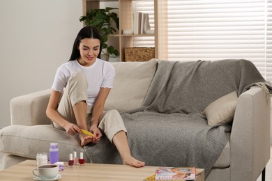 Photo of Beautiful young woman giving herself pedicure in living room