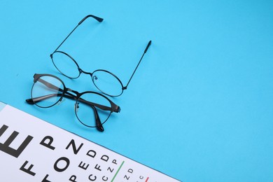 Vision test chart and glasses on light blue background, space for text