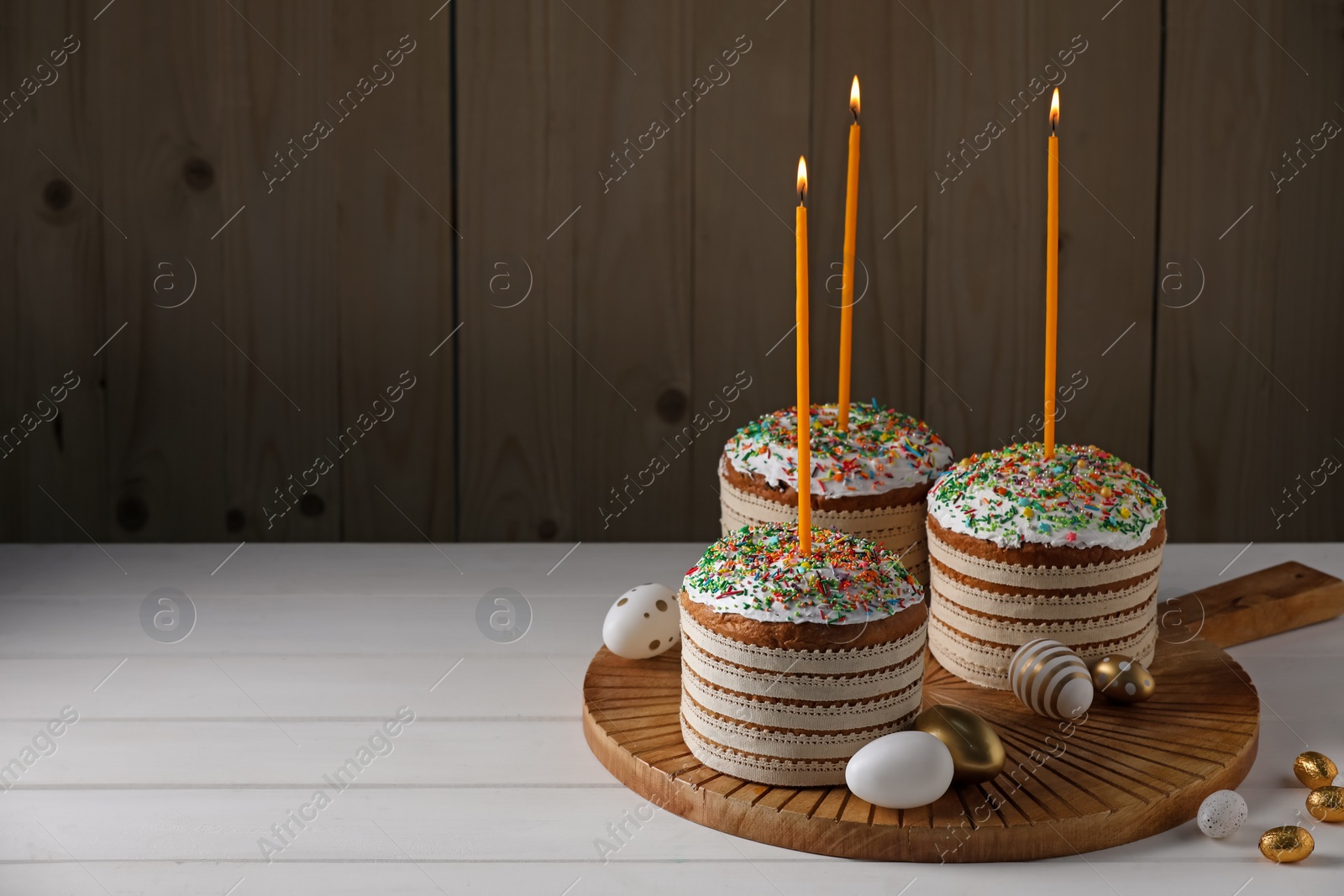Photo of Traditional Easter cakes with sprinkles, candles and decorated eggs on white table. Space for text