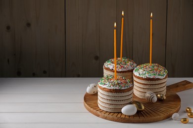 Photo of Traditional Easter cakes with sprinkles, candles and decorated eggs on white table. Space for text