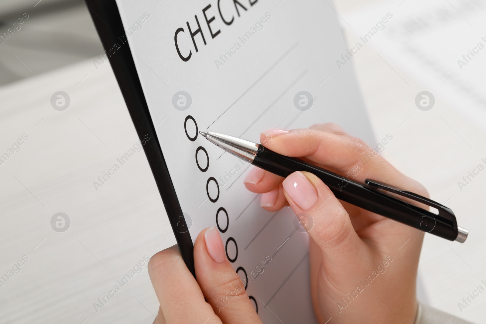 Photo of Woman filling Checklist with pen at table, closeup view