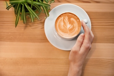 Photo of Woman with cup of aromatic coffee on wooden background, top view